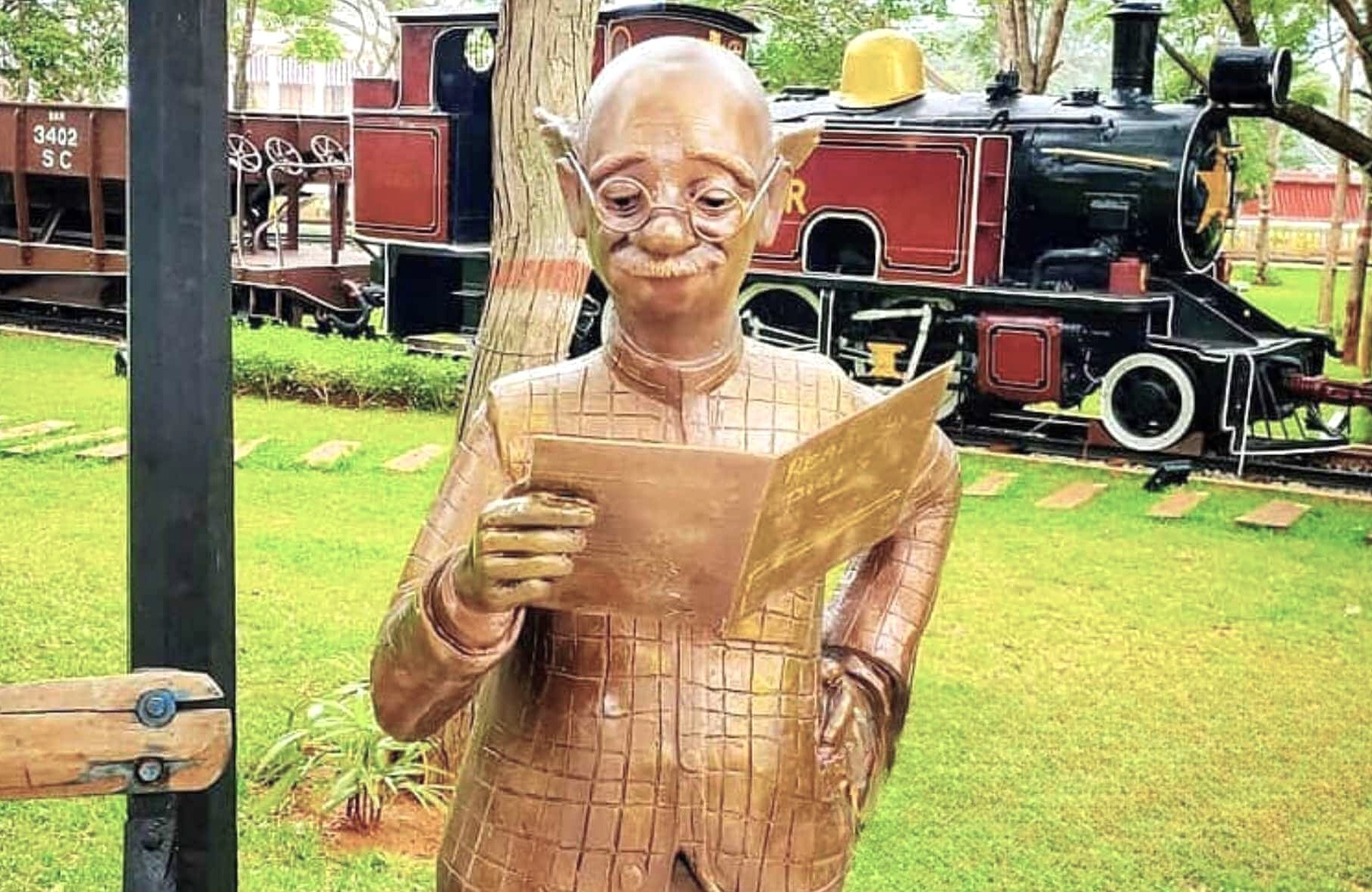 Bronze sculpture of an elderly man reading a document amid vintage train exhibits at the India Railway Museum in Mysore, Karnataka, India, celebrating railway heritage. Bronze sculpture of an elderly man reading a document amid vintage train exhibits at the India Railway Museum in Mysore, Karnataka, India, celebrating railway heritage.