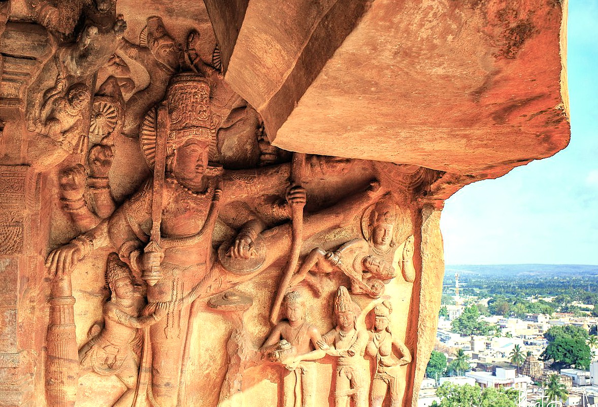 An intricate rock-cut sculpture of a multi-armed Hindu deity, a masterpiece of Chalukyan art, is carved into the sandstone cliffs of the Badami cave temples in Karnataka, India. This stunning carving overlooks the sacred Agastya Lake, near the Pattadakal UNESCO World Heritage site An intricate rock-cut sculpture of a multi-armed Hindu deity, a masterpiece of Chalukyan art, is carved into the sandstone cliffs of the Badami cave temples in Karnataka, India. This stunning carving overlooks the sacred Agastya Lake, near the Pattadakal UNESCO World Heritage site