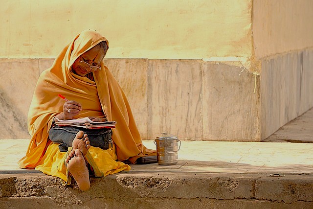 Elderly local woman in saffron robes writing outdoors at the historic Elora and Ajanta Caves near Aurangabad, Maharashtra, India UNESCO World Heritage site, embodying traditional artistry and contemplative cultural heritage.