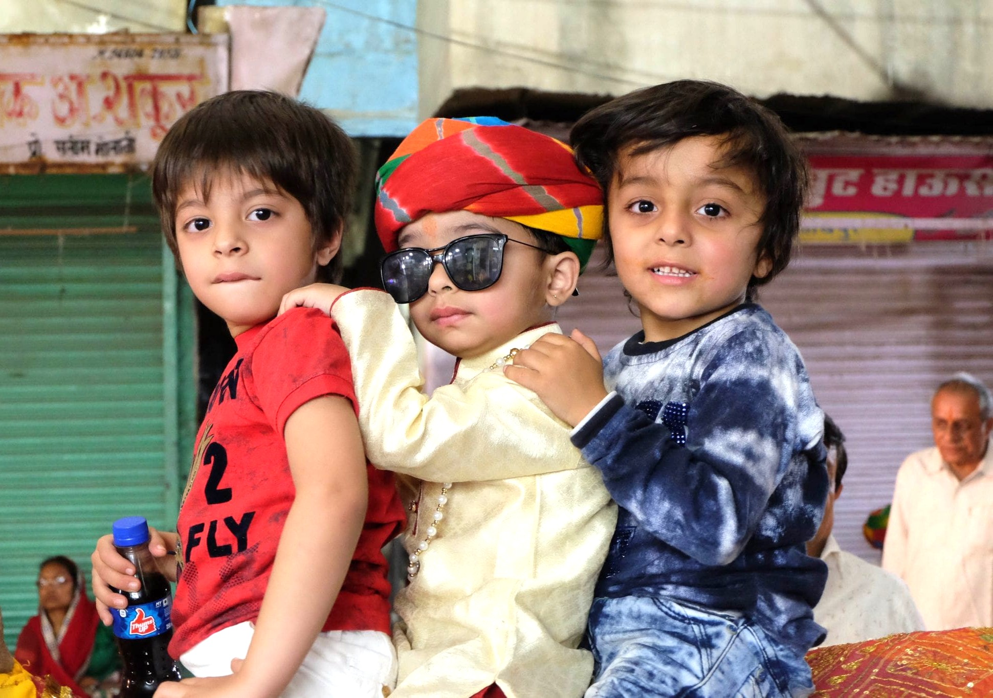 Three young boys, one wearing a vibrant turban and sunglasses, ride a decorated animal during a lively festival in a bustling Jodhpur, Rajasthan marketplace near the Aravali Hills in India. Three young boys, one wearing a vibrant turban and sunglasses, ride a decorated animal during a lively festival in a bustling Jodhpur, Rajasthan marketplace near the Aravali Hills in India.