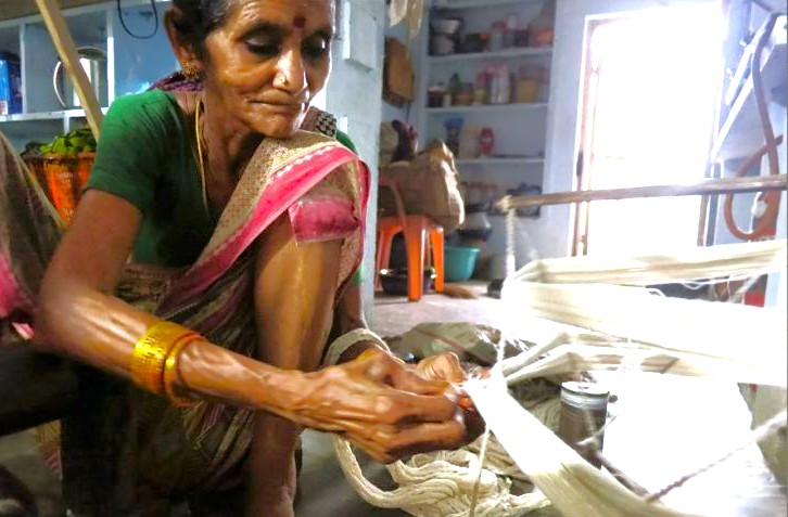 Skilled elderly Indian woman artisan meticulously hand-spinning silk threads in traditional home workshop in Karnataka, India, near Mysore Palace and Bangalore's vibrant Commercial Street shopping and dining, preserving cultural heritage for tourists seeking authentic handicrafts and sustainable experiences. Skilled elderly Indian woman artisan meticulously hand-spinning silk threads in traditional home workshop in Karnataka, India, near Mysore Palace and Bangalore's vibrant Commercial Street shopping and dining, preserving cultural heritage for tourists seeking authentic handicrafts and sustainable experiences.