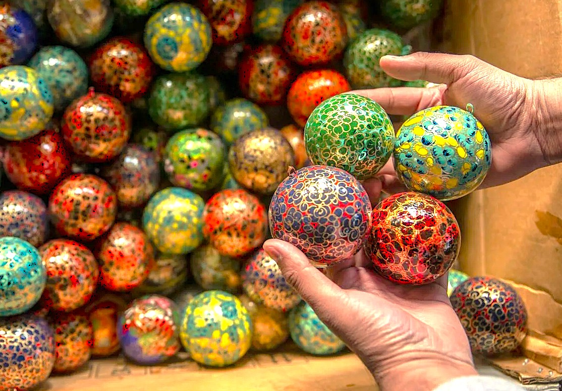 Hands holding colorful hand-painted papier-mâché baubles at Babu Arts and Craft Emporium in Srinagar, Jammu and Kashmir, near saffron fields, Aru Valley, and Betaab Valley.
