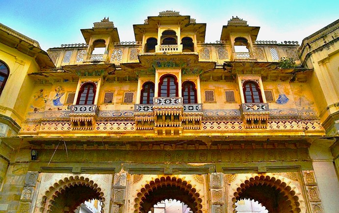 Intricately designed facade of Bagore Ki Haveli in Udaipur, Rajasthan, India, featuring stunning Rajasthani architecture with ornate balconies, detailed frescoes, arched doorways, and vibrant heritage elements under a bright blue sky.
