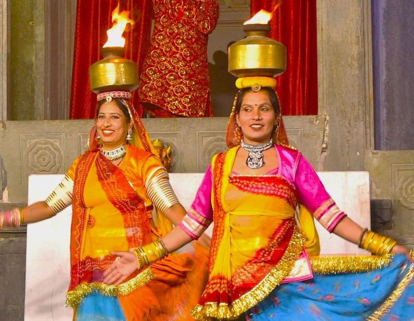 “At Bagore Ki Haveli in Udaipur, Rajasthan, India, women in vibrant Rajasthani attire perform a cultural performance balancing lamps on their heads, showcasing rich heritage with live folk music accompaniment.”
