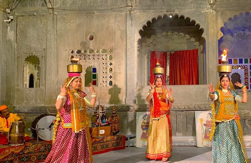 “Women in vibrant Rajasthani attire perform a cultural dance balancing lamps on their heads at Bagore Ki Haveli in Udaipur, Rajasthan, India, showcasing rich heritage with live folk music accompaniment.”