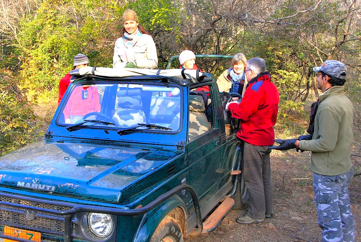 A group of tourists on a wildlife safari in Bandipur National Park tiger reserve in Karnataka, India, exploring lush forest surroundings from an open-top jeep.