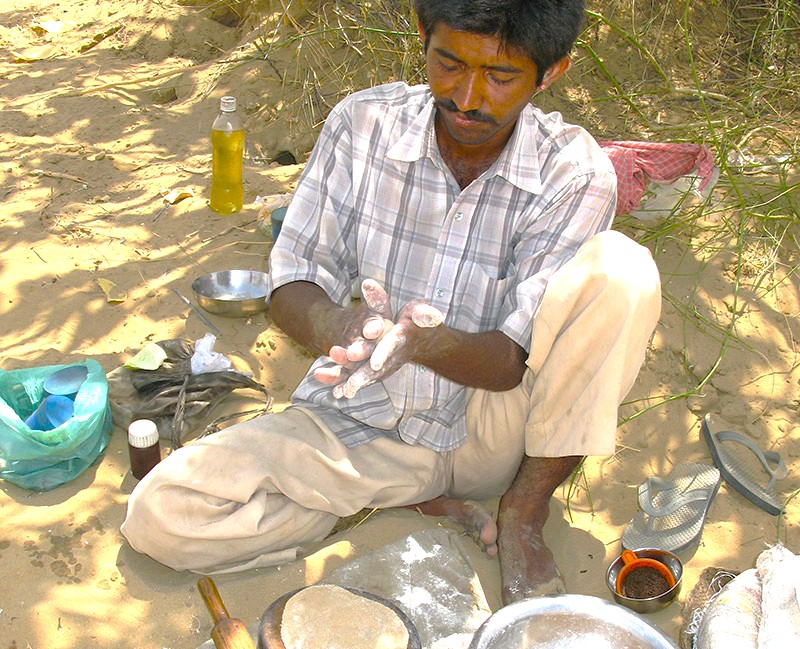 Experience Rajasthani flavors as a local chef hand-rolls chapatis and cooks on golden sand during the Bikaner Camel Safari in the Thar Desert of Rajasthan, India, blending tradition and adventure.
