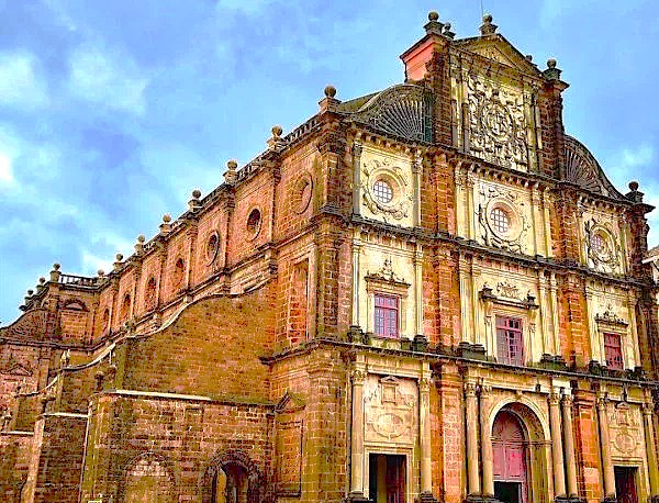 The iconic red laterite stone exterior of the Bom Jesus Basilica, a famous part of the Old Goa Unesco churches, stands under a cloudy sky in Goa, India.
