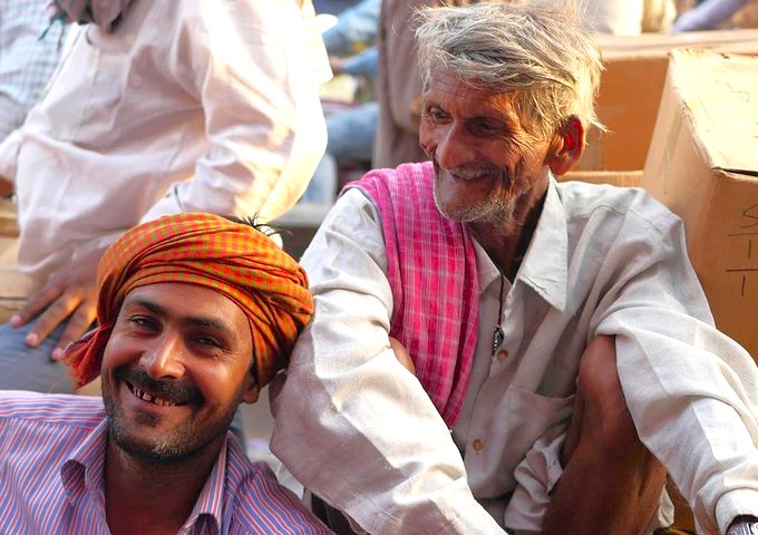 Two smiling local men wearing traditional turbans and scarves in India-Chandi Chowk New Delhi, enjoying vibrant market camaraderie amid colorful spice stalls, textile vendors, auto-rickshaws, historic architecture, lively heritage atmosphere. Two smiling local men wearing traditional turbans and scarves in India-Chandi Chowk New Delhi, enjoying vibrant market camaraderie amid colorful spice stalls, textile vendors, auto-rickshaws, historic architecture, lively heritage atmosphere.