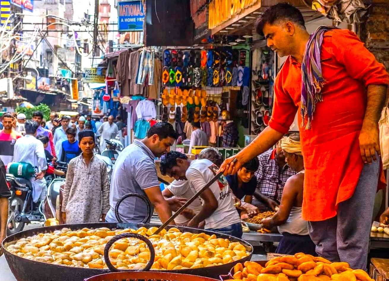 Two smiling local men wearing traditional turbans and scarves in India-Chandi Chowk New Delhi, enjoying vibrant market camaraderie amid colorful spice stalls, textile vendors, auto-rickshaws, historic architecture, lively heritage atmosphere. Two smiling local men wearing traditional turbans and scarves in India-Chandi Chowk New Delhi, enjoying vibrant market camaraderie amid colorful spice stalls, textile vendors, auto-rickshaws, historic architecture, lively heritage atmosphere.