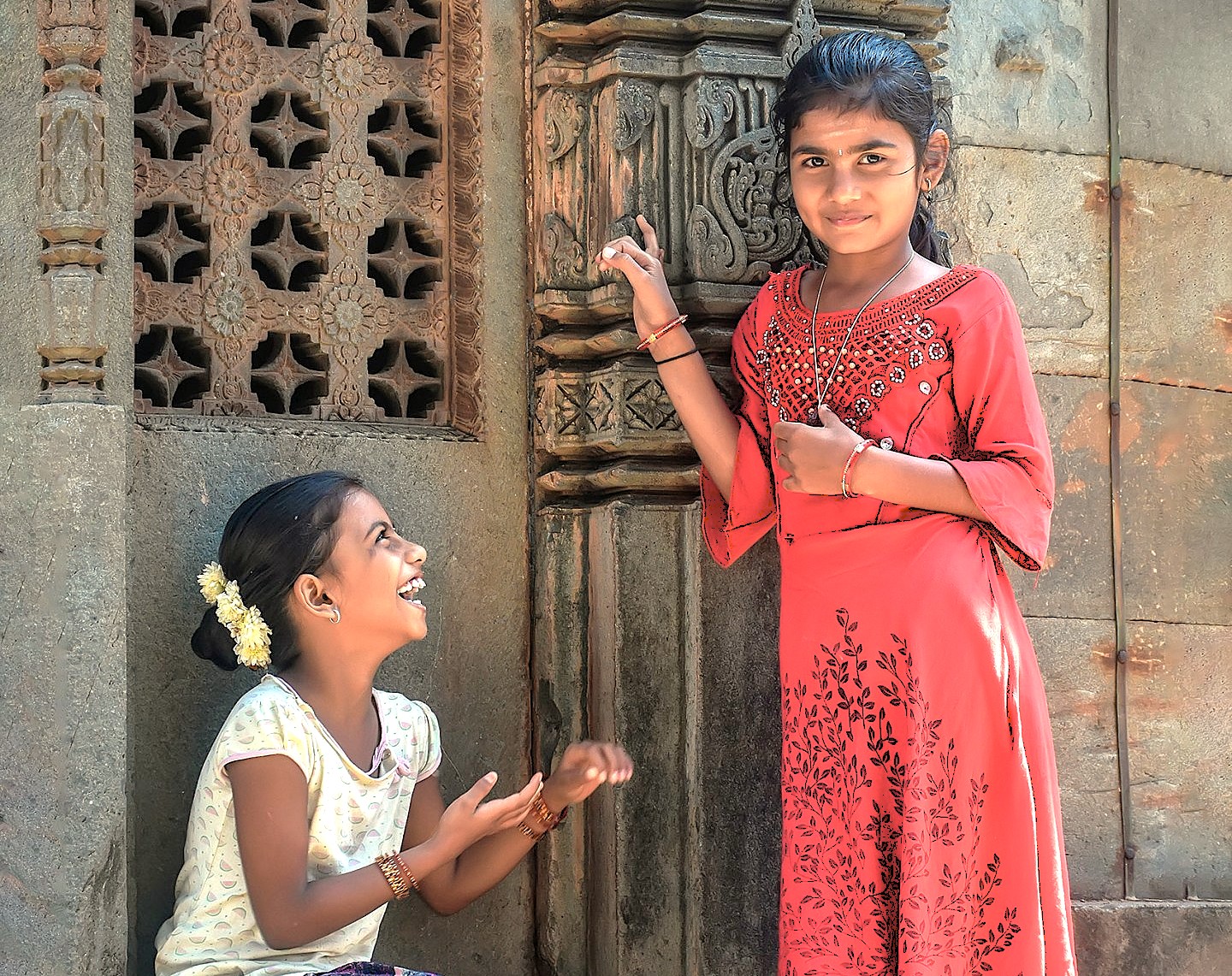 Local girls smile by the carved stone walls of Chandramouli Temple in Hubli, Karnataka, India, near Agadi Thota Village on the way to Old Goa Unesco churches. Local girls smile by the carved stone walls of Chandramouli Temple in Hubli, Karnataka, India, near Agadi Thota Village on the way to Old Goa Unesco churches.