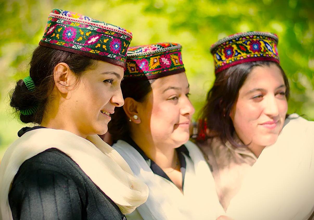 Three smiling Kashmiri women in traditional embroidered caps showcase the vibrant local culture and heritage near Chinar Bagh Ghat in Srinagar, Jammu and Kashmir, India.