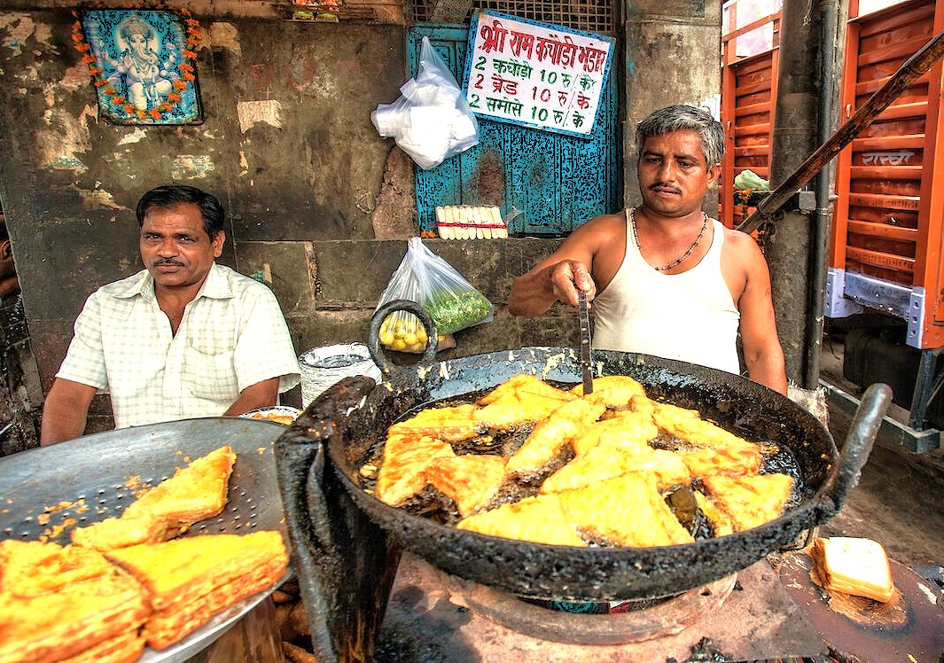Local street food vendors fry fresh snacks in a large kadai, a popular culinary experience for tourists near Chinar Bagh Ghat in Srinagar, Jammu and Kashmir, India.