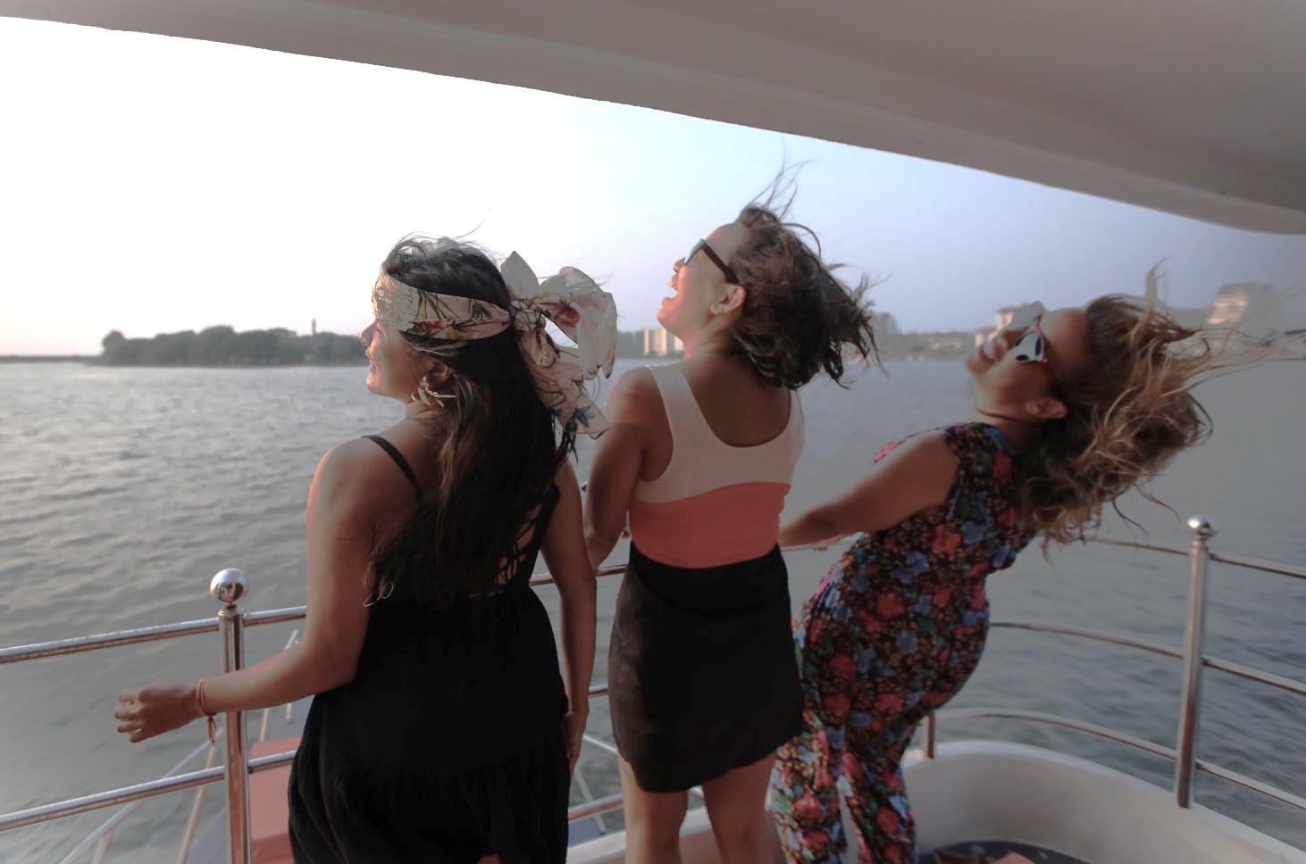 Three women laughing on a boat ride near Chowpatty Beach in Mumbai, Mahapradesh, India, enjoying sunset views over Marine Drive waterway with vibrant city skyline and serene, relaxing coastal adventure.