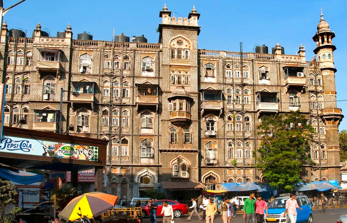 Historic colonial-era building and bustling street stalls line Colaba Causeway in Mumbai, Maharashtra, India, showcasing vibrant commercial activity with pedestrians, colorful umbrellas, street vendors, vehicles, cultural heritage, and sunny ambiance. Historic colonial-era building and bustling street stalls line Colaba Causeway in Mumbai, Maharashtra, India, showcasing vibrant commercial activity with pedestrians, colorful umbrellas, street vendors, vehicles, cultural heritage, and sunny ambiance.