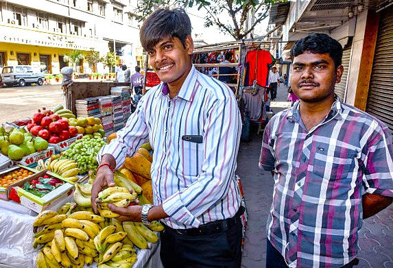Two smiling fruit vendors display fresh bananas and apples at a bustling Colaba Causeway street market in Mumbai, India, showcasing local produce, vibrant community interaction, Mahapradesh cultural heritage, and commerce. Two smiling fruit vendors display fresh bananas and apples at a bustling Colaba Causeway street market in Mumbai, India, showcasing local produce, vibrant community interaction, Mahapradesh cultural heritage, and commerce.