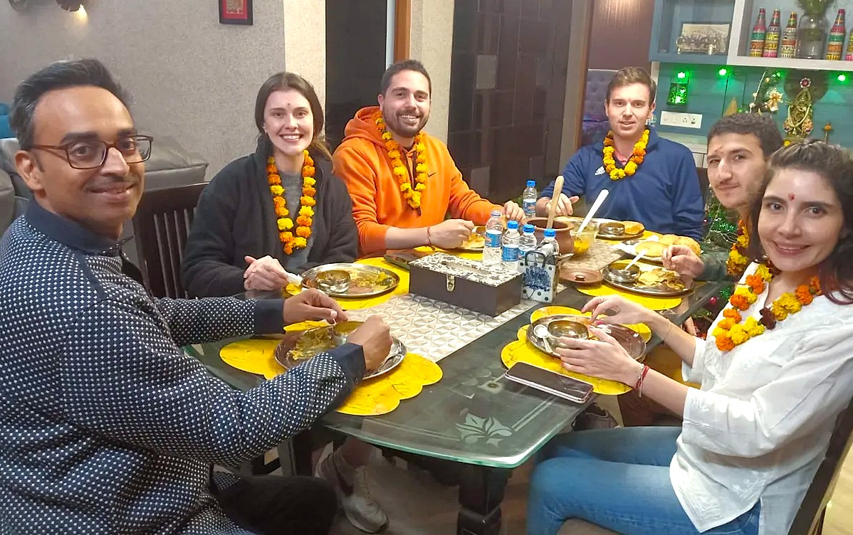 “Seven smiling participants wearing marigold garlands share a traditional Indian meal at hands-on India cooking classes workshop, exploring authentic regional flavors and exciting culinary techniques.”  “Seven smiling participants wearing marigold garlands share a traditional Indian meal at hands-on India cooking classes workshop, exploring authentic regional flavors and exciting culinary techniques.”