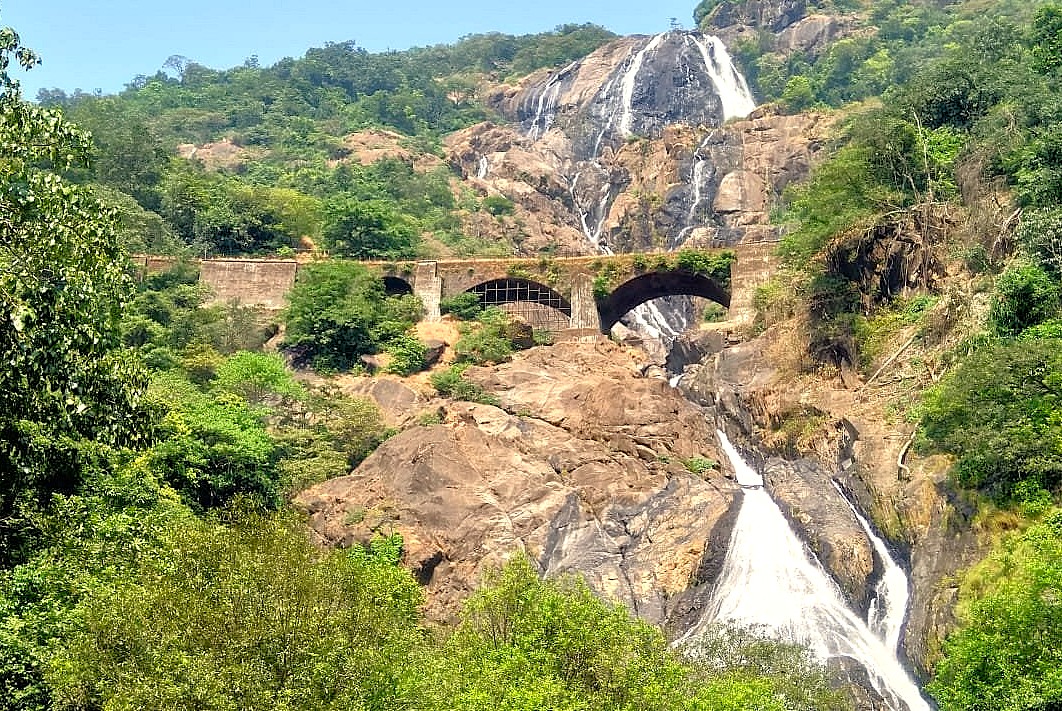 Witness the iconic railway bridge crossing the spectacular Dudhsagar Falls in India. This breathtaking waterfall is a popular destination, often reached by an adventurous Jeep Safari, for travellers on a road trip from the UNESCO Hampi site in Karnataka to Goa. Witness the iconic railway bridge crossing the spectacular Dudhsagar Falls in India. This breathtaking waterfall is a popular destination, often reached by an adventurous Jeep Safari, for travellers on a road trip from the UNESCO Hampi site in Karnataka to Goa.