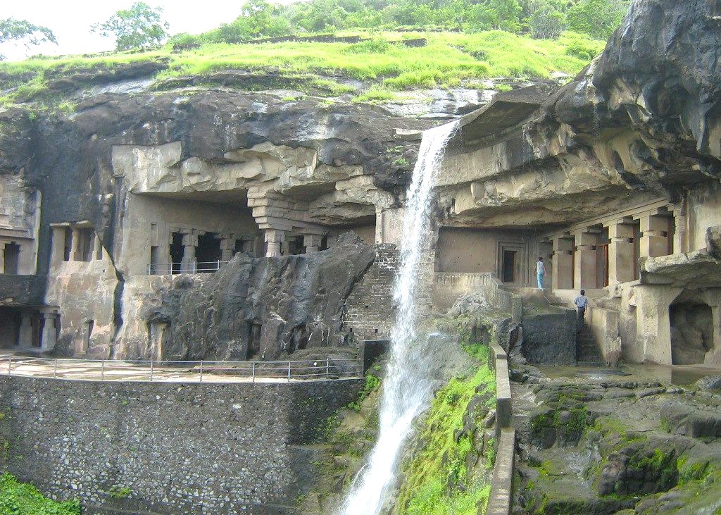 A cascading waterfall flows past ancient rock-cut chambers of the UNESCO-listed Elephanta Caves on Elephanta Island near Mumbai in Mahapradesh, India, surrounded by verdant hills, historic carvings, archaeological landmark, pathways. A cascading waterfall flows past ancient rock-cut chambers of the UNESCO-listed Elephanta Caves on Elephanta Island near Mumbai in Mahapradesh, India, surrounded by verdant hills, historic carvings, archaeological landmark, pathways.