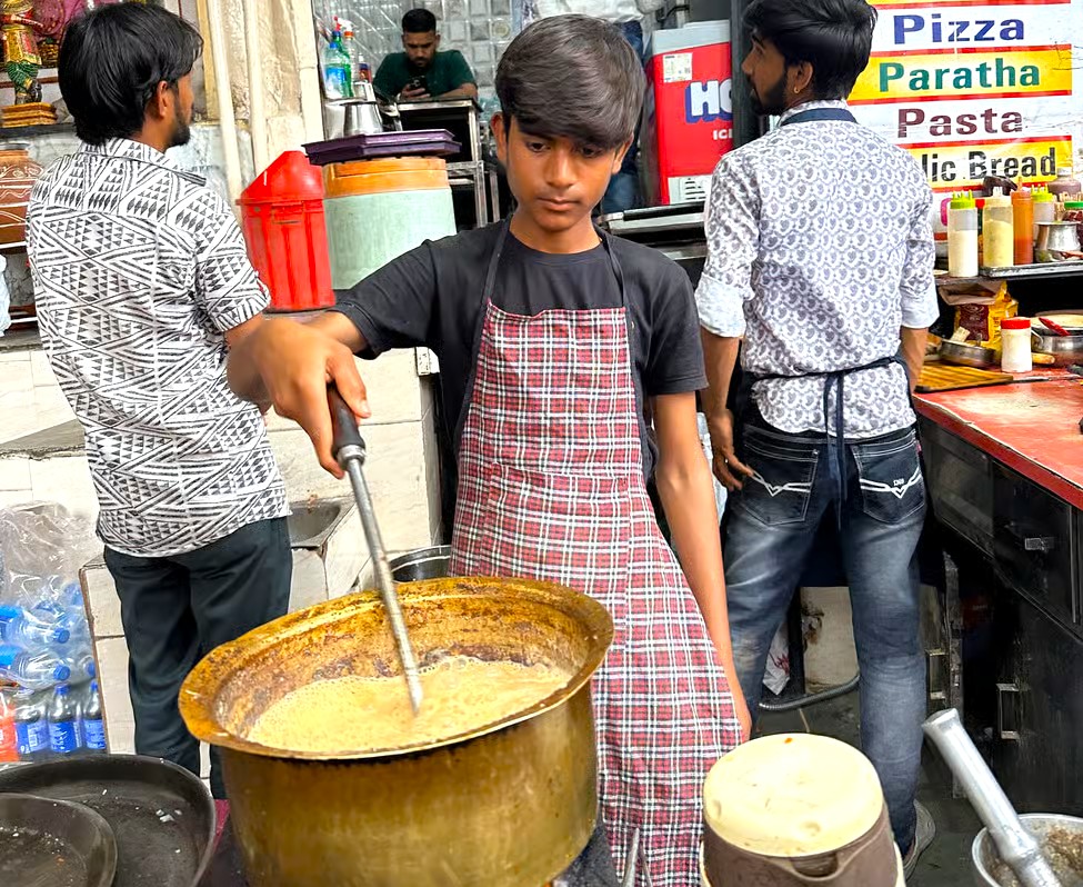 Vibrant Indian street food stall near Sri Elkingi Temple in Udaipur, Rajasthan features a young boy stirring masala curry in a brass pot, colorful condiments, parathas, bustling local culinary culture. Vibrant Indian street food stall near Sri Elkingi Temple in Udaipur, Rajasthan features a young boy stirring masala curry in a brass pot, colorful condiments, parathas, bustling local culinary culture.