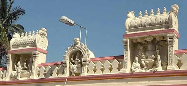 Ornate white stone carvings of mythological figures adorn the upper facade of a Hindu temple in Bangalore, Karnataka, India, blending traditional South Indian temple architecture with vibrant modern urban surroundings. Ornate white stone carvings of mythological figures adorn the upper facade of a Hindu temple in Bangalore, Karnataka, India, blending traditional South Indian temple architecture with vibrant modern urban surroundings.