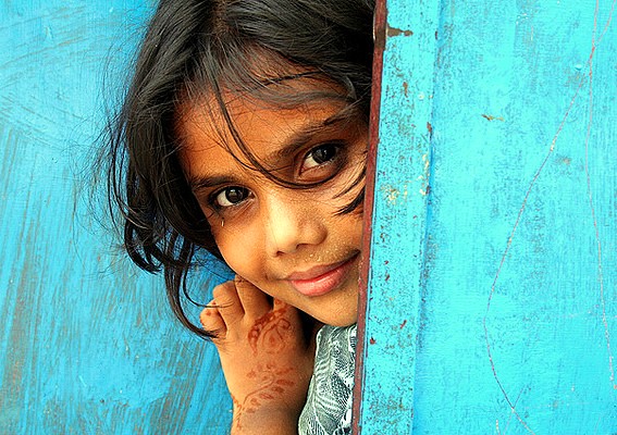 A young local girl with henna on her hand peeks from behind a blue door in Goa, India. This region, famous for its Goa Beaches, is located near Karnataka and the historic Old Goa St. Francis Church UNESCO churches. A young local girl with henna on her hand peeks from behind a blue door in Goa, India. This region, famous for its Goa Beaches, is located near Karnataka and the historic Old Goa St. Francis Church UNESCO churches.
