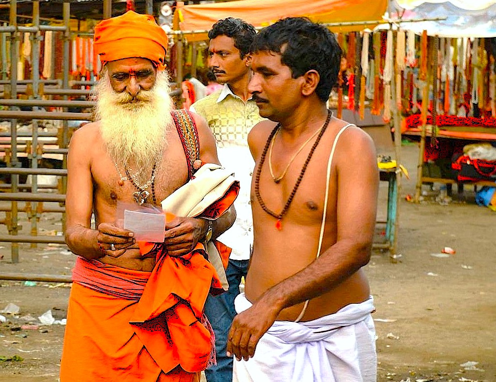 Three local pilgrims converse near bustling Grishneshwar Temple stalls in Aurangabad, Maharashtra, India, framed against the UNESCO-listed Ellora and Ajanta Caves backdrop, capturing vibrant culture, smiling devotees, and sacred heritage.