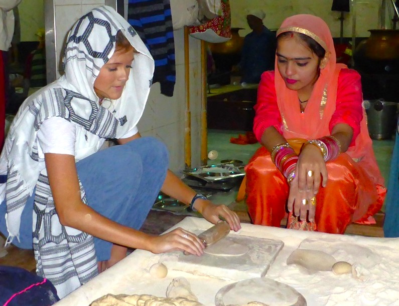 A volunteer instructs a tourist in traditional roti making at India New Delhi Gurudwara Bangla Sahib Sikh Temple’s open kitchen, highlighting community service, cultural exchange, and shared spiritual langar preparation. A volunteer instructs a tourist in traditional roti making at India New Delhi Gurudwara Bangla Sahib Sikh Temple’s open kitchen, highlighting community service, cultural exchange, and shared spiritual langar preparation.
