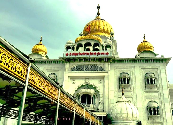 A view of the grand white façade and golden domes of Gurudwara Bangla Sahib Sikh Temple in New Delhi, India, framed by detailed carvings, representing sacred heritage and spiritual devotion. A view of the grand white façade and golden domes of Gurudwara Bangla Sahib Sikh Temple in New Delhi, India, framed by detailed carvings, representing sacred heritage and spiritual devotion.