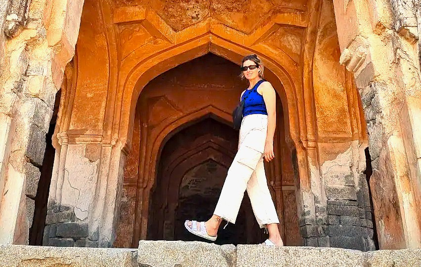 A tourist explores the ancient stone archways of the Hampi UNESCO site in Karnataka, India, home to the famous Vittala Temple and the historic Elephant Stables.