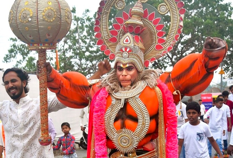 Elaborate Hanuman festival performer in vibrant costume dances before a cheering crowd near New Delhi’s iconic Hanuman Mandir during India’s cultural celebration, showcasing intricate jewelry, dynamic pose, and community spirit.