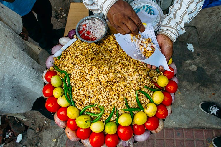 Vibrant bustling street food display of seasoned popcorn garnished with tomatoes, lemons and green chilies stands outside Hanuman Mandir in New Delhi, India, showcasing authentic local culinary culture, temple surroundings.