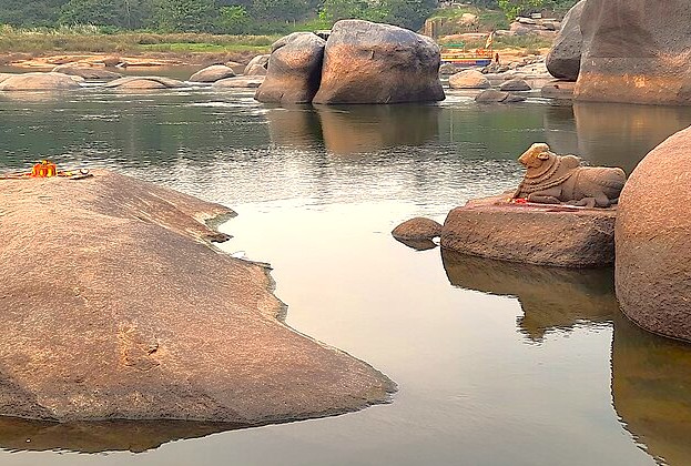The Tungabhadra River near Hippy Island features a Nandi statue amidst ancient boulders. This picturesque landscape links the Hampi, Karnataka, India UNESCO site clusters including Hemakuta Hill, the Queens' Bath, and the Elephant Stables ruins. The Tungabhadra River near Hippy Island features a Nandi statue amidst ancient boulders. This picturesque landscape links the Hampi, Karnataka, India UNESCO site clusters including Hemakuta Hill, the Queens' Bath, and the Elephant Stables ruins.