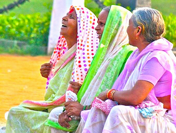 Three elderly Indian women in colorful traditional sarees share joyous laughter outdoors against lush greenery near Delhi’s iconic India Gate, India, capturing cultural camaraderie, vibrant attire, rural charm, and friendship. Three elderly Indian women in colorful traditional sarees share joyous laughter outdoors against lush greenery near Delhi’s iconic India Gate, India, capturing cultural camaraderie, vibrant attire, rural charm, and friendship.