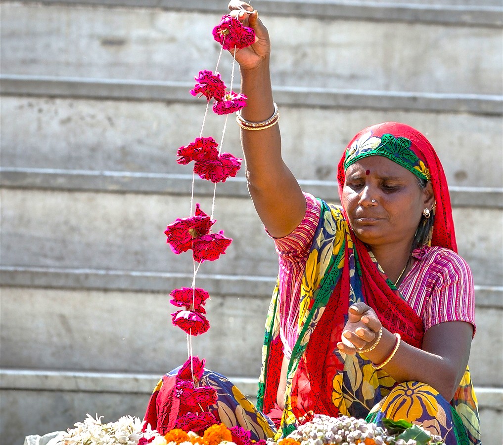 Local woman offers flower garlands during ritual at UNESCO-listed Jagdish Temple steps in Udaipur, Rajasthan, India, reflecting vibrant cultural heritage, sacred tradition, rich community devotion, and historic Hindu worship practice.