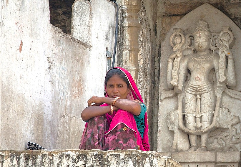 Portrait of a Rajasthani woman clad in vibrant traditional attire seated beside intricate stone carvings at Udaipur’s historic UNESCO-recognized Jagdish Temple in Rajasthan, India, reflecting rich cultural heritage and devotion.