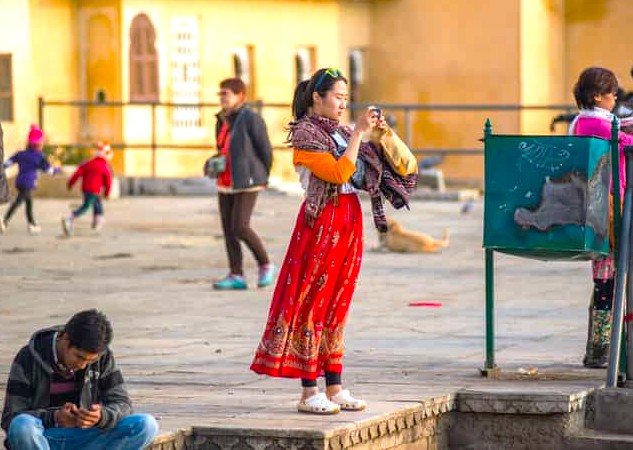 Captivating shot of a young tourist photographing the historic Jagdish Temple in Udaipur, Rajasthan, India, amidst playful local children and relaxed visitors, highlighting UNESCO heritage charm and vibrant cultural atmosphere.