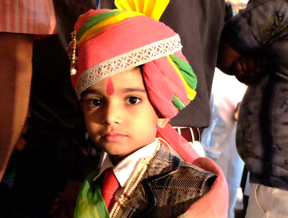 Young boy in colorful traditional turban and formal attire poses at a vibrant festive street ceremony in Jaipur, Rajasthan, India, highlighting local culture, celebratory mood, authentic traditions, and heritage craftsmanship.