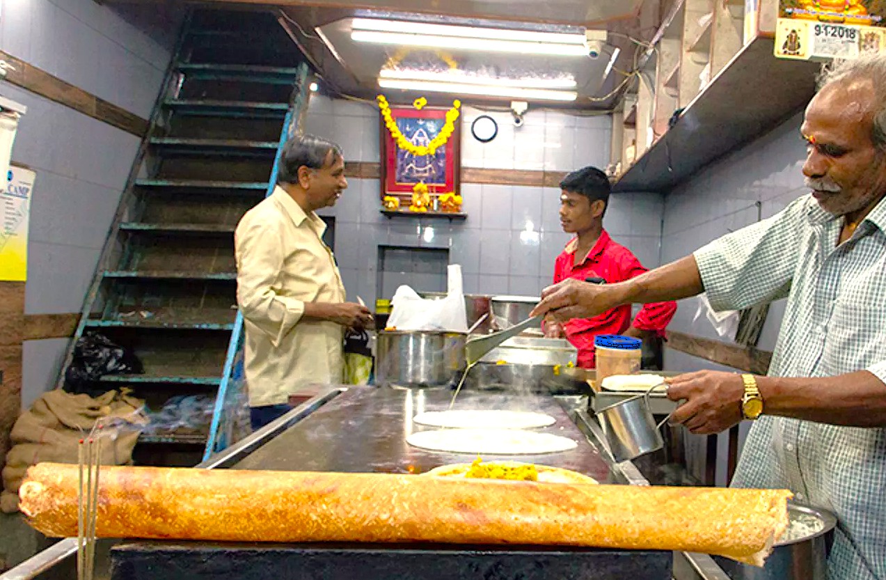 A local vendor prepares delicious South Indian street food for tourists visiting the Jatayu Sculpture and the ancient Lepakshi Temple, famous for its mysterious floating pillar, in Andhra Pradesh, India.