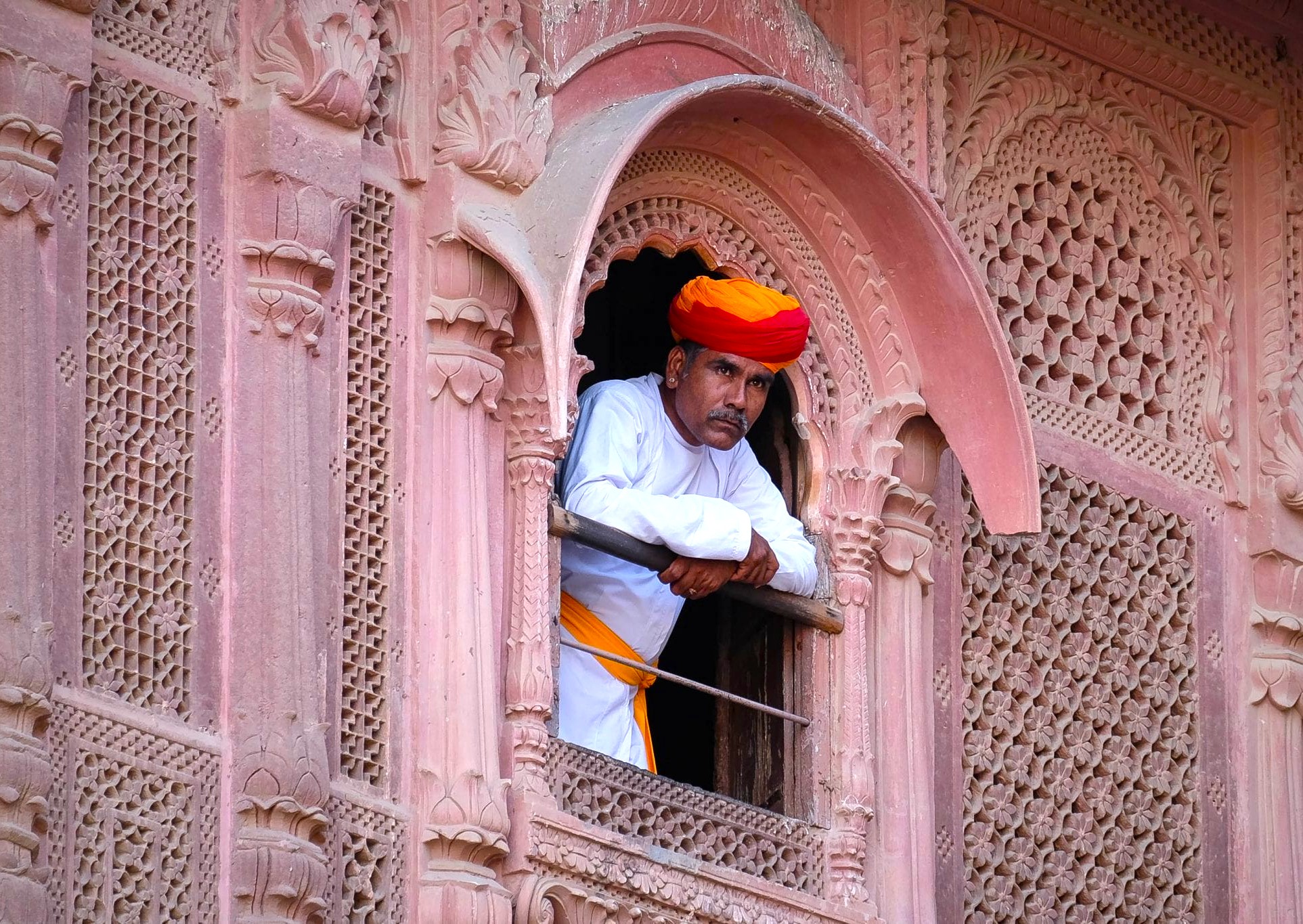 A Rajasthani man in traditional attire looks out from an intricately carved window in Jodhpur, Rajasthan, India. The blue city is famous for its historic architecture and vibrant cultural heritage. A Rajasthani man in traditional attire looks out from an intricately carved window in Jodhpur, Rajasthan, India. The blue city is famous for its historic architecture and vibrant cultural heritage.