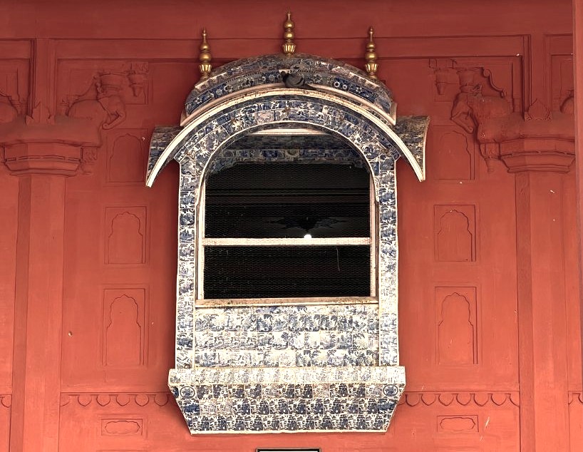 Ornate blue-tiled architectural window overlooking vibrant red fort walls at Junagarh Fort Bikaner, showcasing Rajasthan’s heritage and cultural depth on India’s Thar Desert edge, blending Mughal motifs, intricate relief patterns. Ornate blue-tiled architectural window overlooking vibrant red fort walls at Junagarh Fort Bikaner, showcasing Rajasthan’s heritage and cultural depth on India’s Thar Desert edge, blending Mughal motifs, intricate relief patterns.