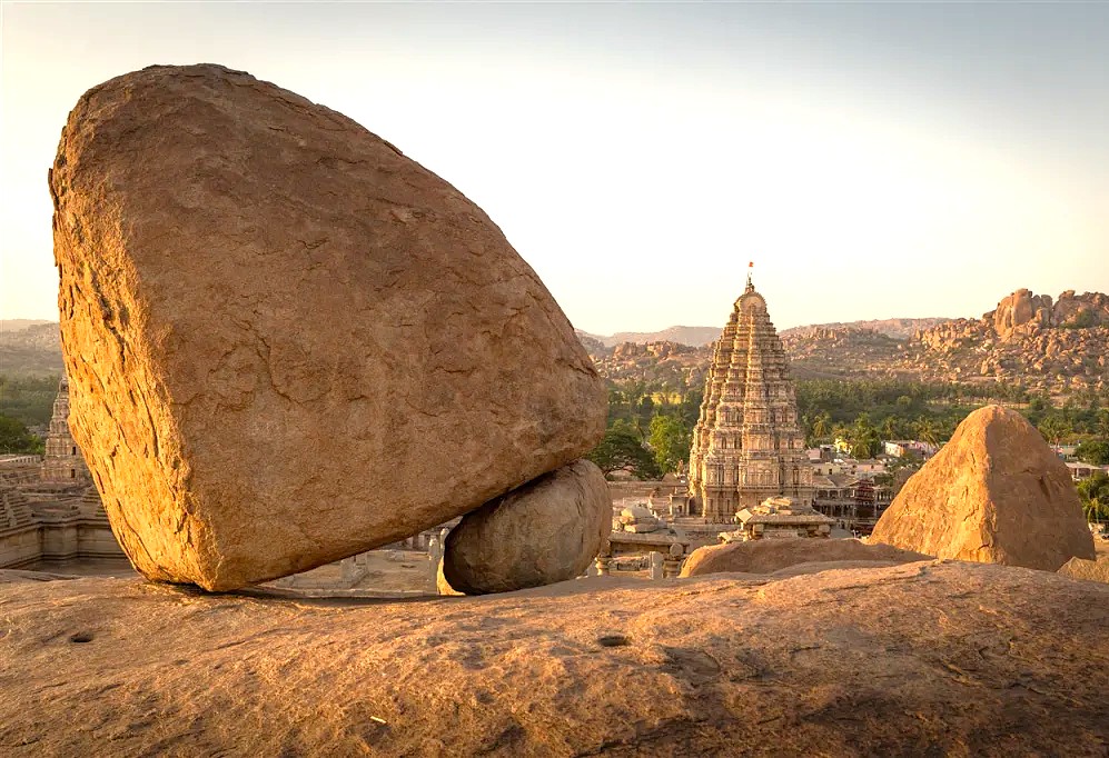The iconic balance rock stands near the towering Virupaksha Temple, showcasing the unique geological landscape surrounding the Kadalekalu Ganesha at the UNESCO site of Hampi, Karnataka, India. The iconic balance rock stands near the towering Virupaksha Temple, showcasing the unique geological landscape surrounding the Kadalekalu Ganesha at the UNESCO site of Hampi, Karnataka, India.
