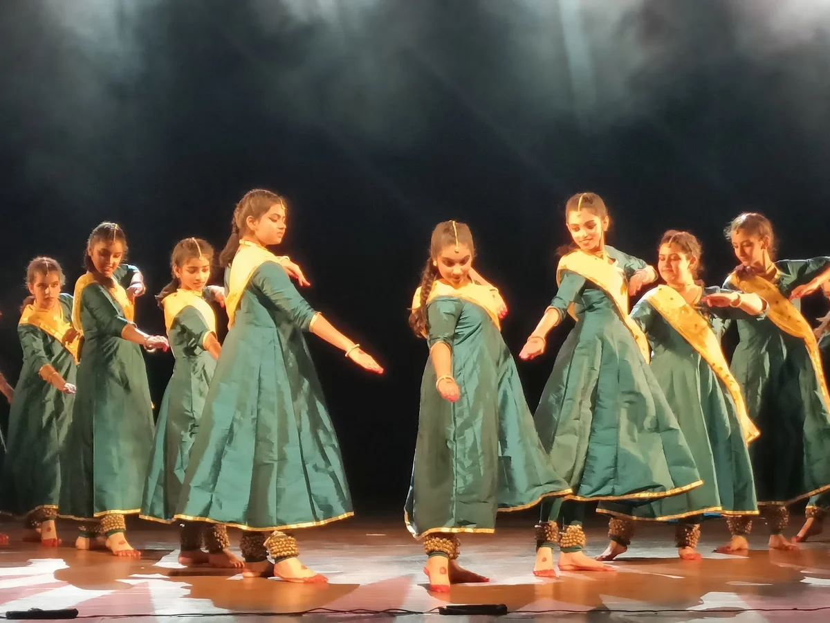 Young Indian classical dancers in synchronized formation wearing green and gold traditional attire perform a vibrant, graceful rhythmic cultural dance under dramatic stage lighting at Karmani Auditorium in Delhi, India. Young Indian classical dancers in synchronized formation wearing green and gold traditional attire perform a vibrant, graceful rhythmic cultural dance under dramatic stage lighting at Karmani Auditorium in Delhi, India.