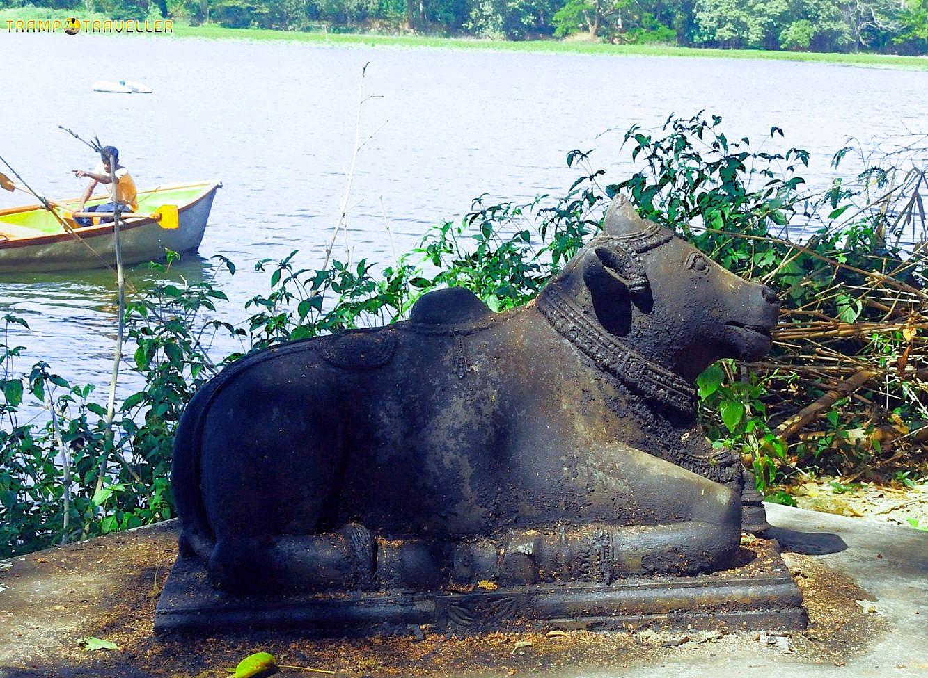 "Weathered stone Nandi bull statue at Karanji Lake in Mysore Karnataka India beside serene waters with boating activity, lush greenery framing cultural heritage and tranquility."