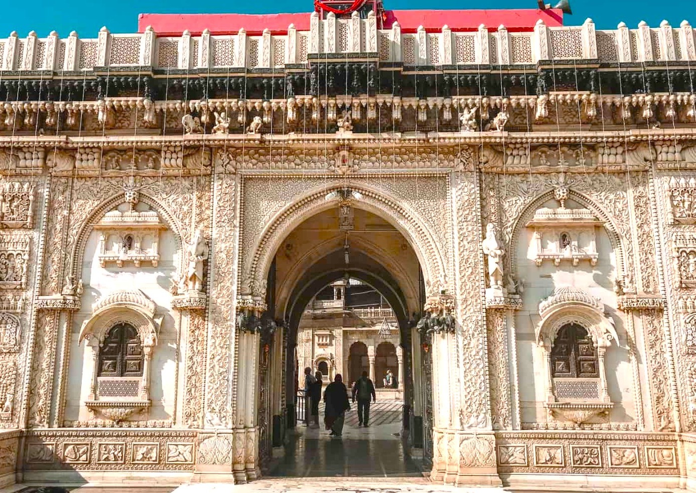 Ornate carved archway of Karni Mata Rat Temple in Bikaner’s Thar Desert, Rajasthan, India, welcomes pilgrims through intricate stone sculptures, floral motifs, and Rajasthani architectural details at historic religious gateway.