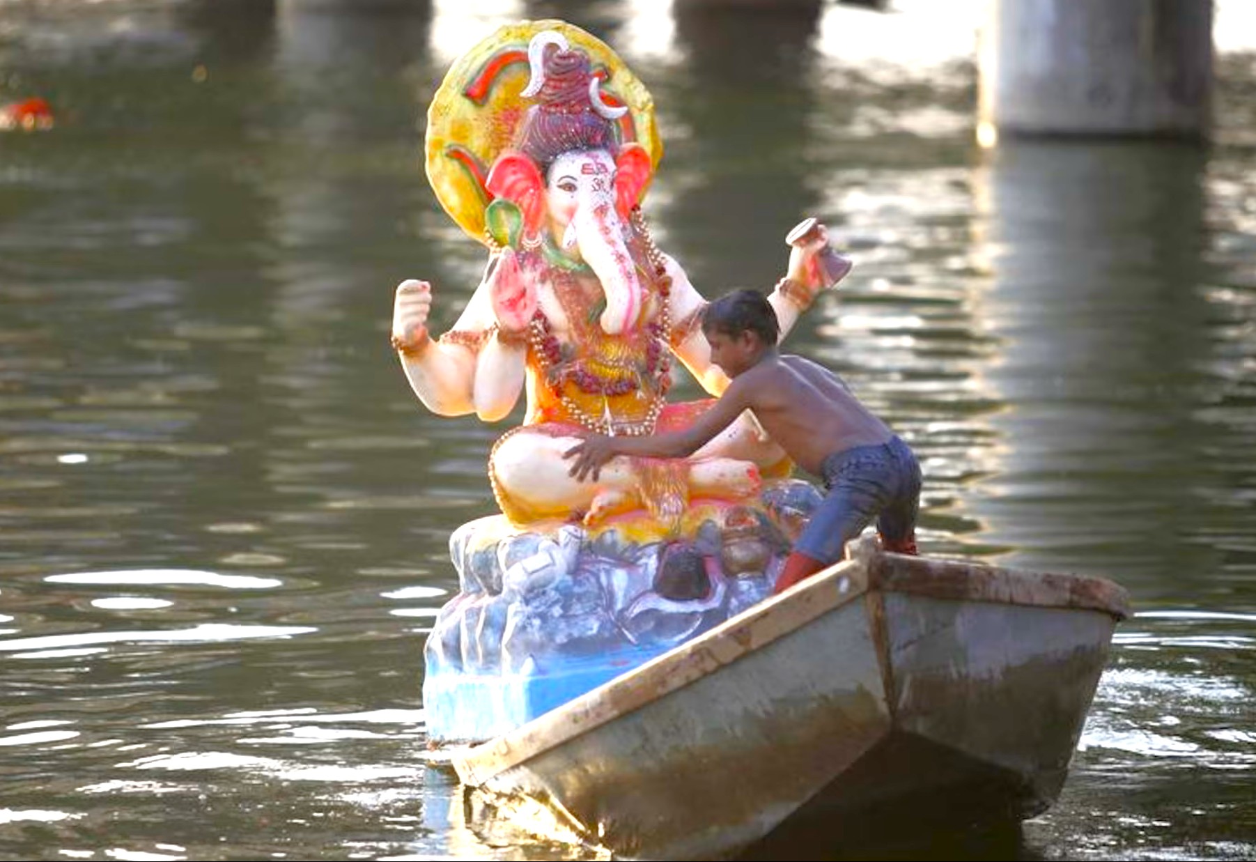 A young devotee guides a colorful Lord Ganesha idol on a wooden boat during immersion ceremony in Kochi backwaters, Kerala, South India, blending religious tradition, cultural devotion, and scenic waterways.