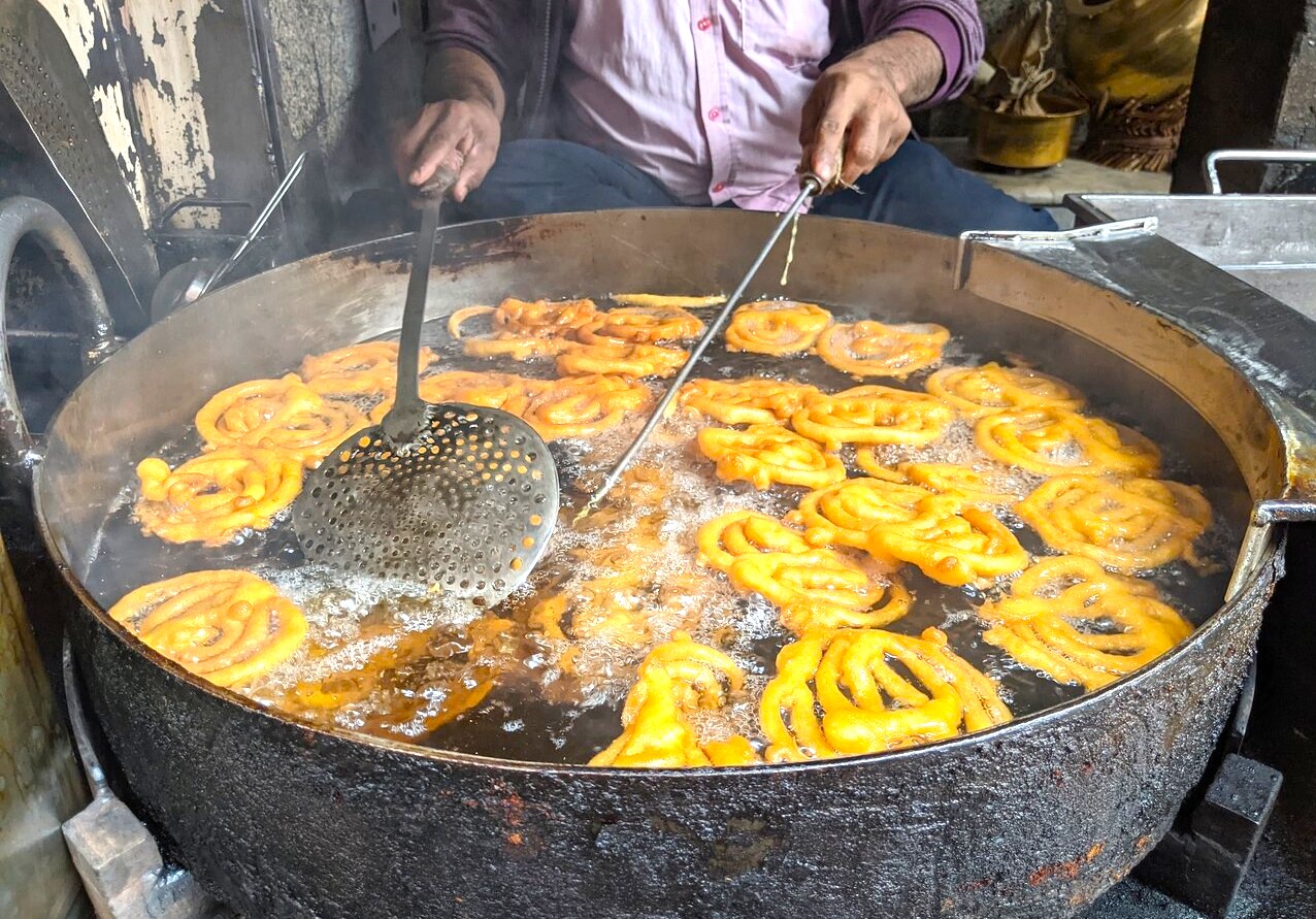 Golden jalebi spirals sizzling in hot oil at a bustling street food stall in Kochi, Kerala, South India, showcasing traditional Indian sweets, local cuisine and authentic Kerala street food experience.