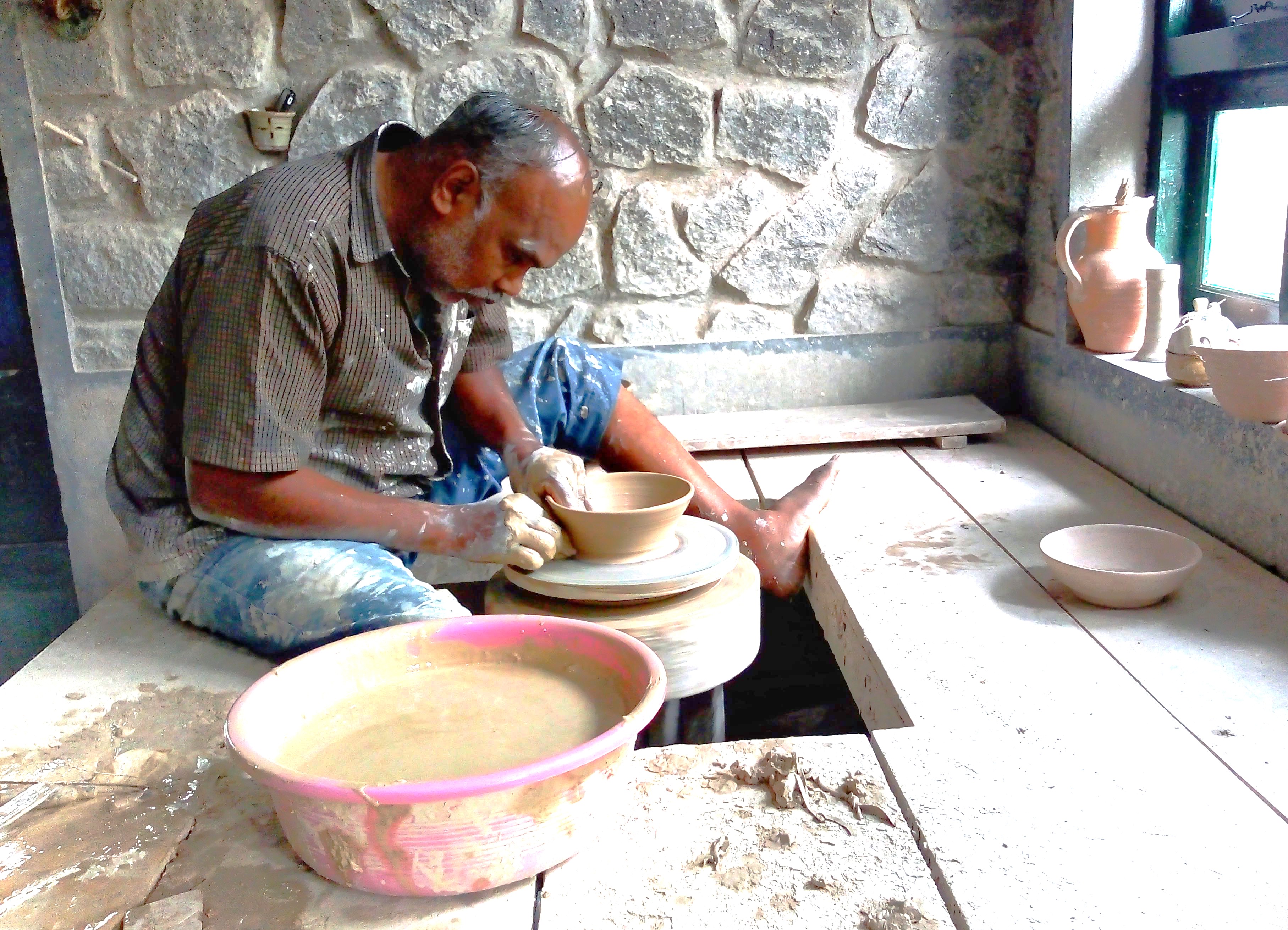 Experienced artisan shaping clay on a traditional pottery wheel in Kodaikanal’s Palani Hills workshop, South India, Tamil Nadu, showcasing ancient craftsmanship amidst picturesque mountain scenery.
