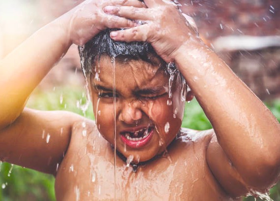 A young boy enjoys an outdoor shower under fresh mountain springs in Kodaikanal’s Palani Hills, Tamil Nadu, South India, embracing nature’s purity with refreshing joy.