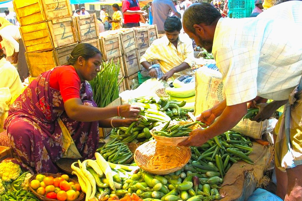 Woman vendor offering fresh okra and assorted vegetables at the bustling Sunday Markets in Kodaikanal, Palani Hills, Tamil Nadu, South India, under vibrant market tents.